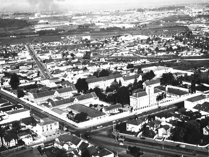 Final da década de 1950 - Vista aérea do conjunto arquitetônico do Hospício Nossa Senhora da Luz.Fonte: Pontifícia Universidade Católica do Paraná.Ao fundo, o bairro do Guabirotuba.